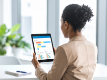 Eine Compliance-Verantwortliche Eine Compliance-Verantwortliche sitzt an einem Schreibtisch und betrachtet auf einem Tablet statistische Auswertungen zu eingegangenen Meldungen auf einem Dashboard.