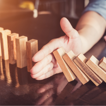 Une surcharge d'outils : Trop de programmes, pas d'intégration et des coûts croissants La main arrête la chute des dominos - symbole d'un trop grand nombre de solutions individuelles et d'un manque d'intégration des systèmes.