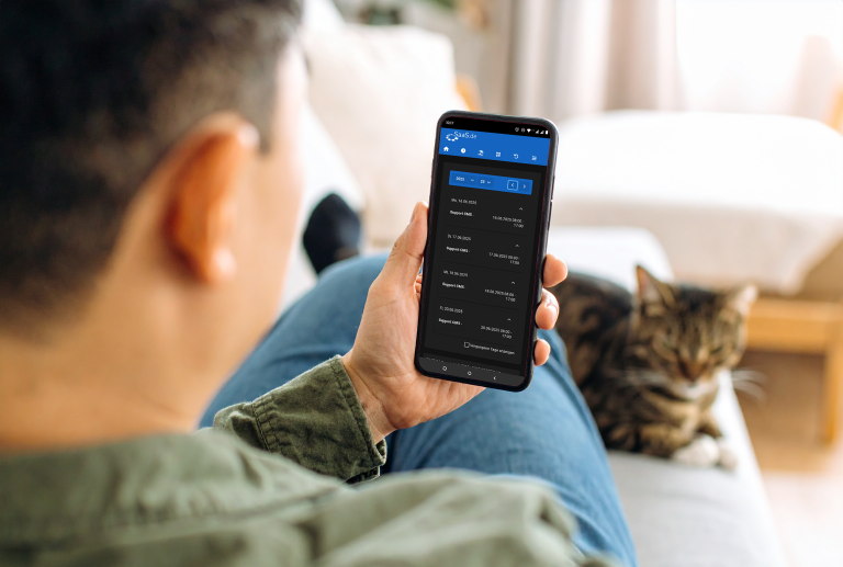 Ein Mann sitzt entspannt auf einem Sofa mit einem Smartphone in der Hand, auf dem ein digitaler Schichtplan der Plattform „SaaS.de“ angezeigt wird. Neben ihm liegt eine getigerte Katze. Der Schichtplan zeigt Einträge für „Support CMS“ an mehreren Tagen im Juni 2025.